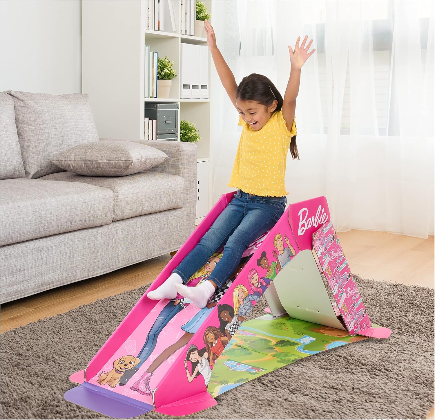 Child playing on a Barbie-themed inflatable slide in a living room.