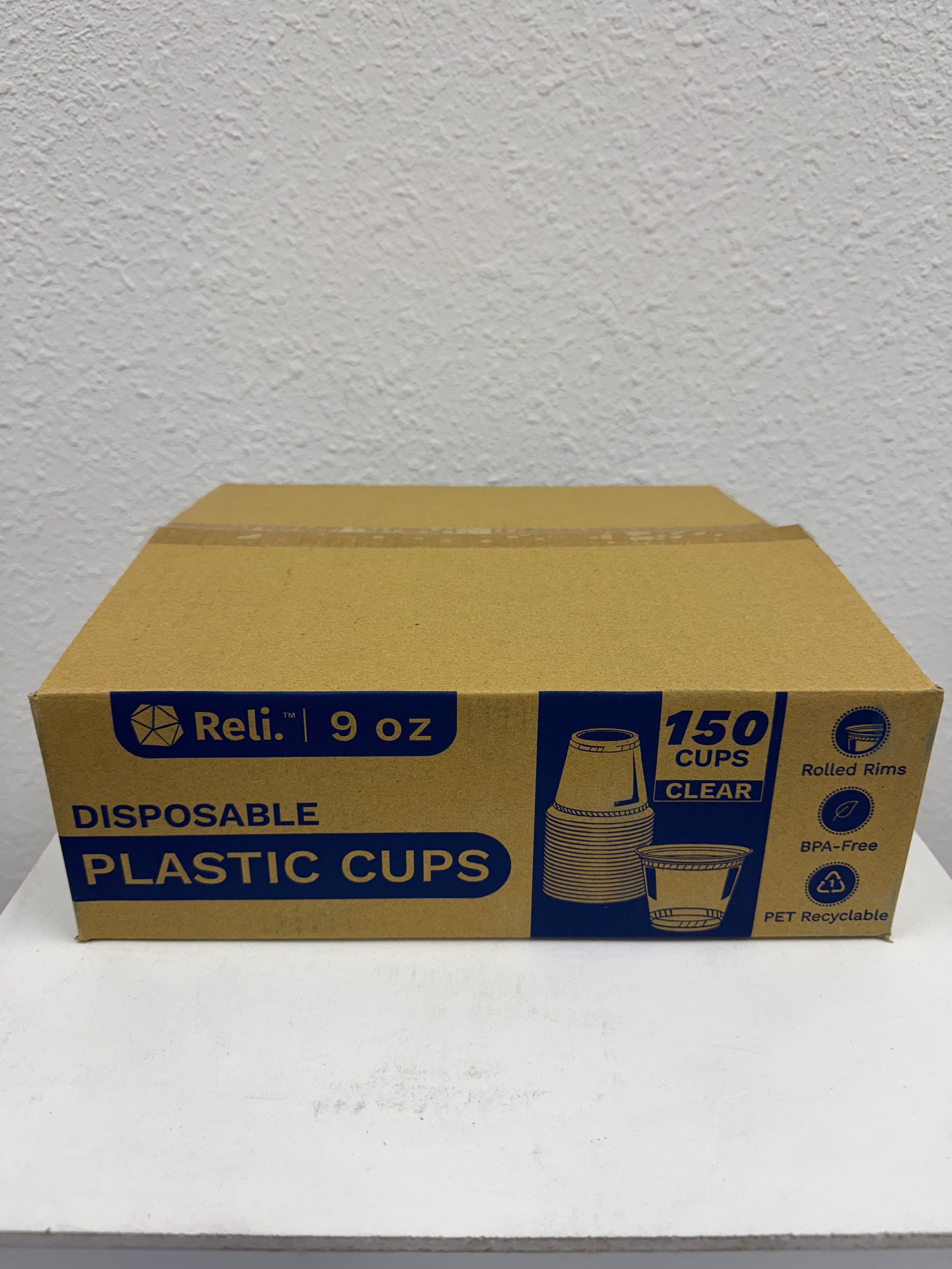 Box of Reli disposable plastic cups on a white surface with a gray textured wall background